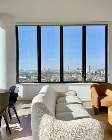 Open-plan apartment with dining table, brown leather sofa, and floor-to-ceiling windows overlooking city skyline
